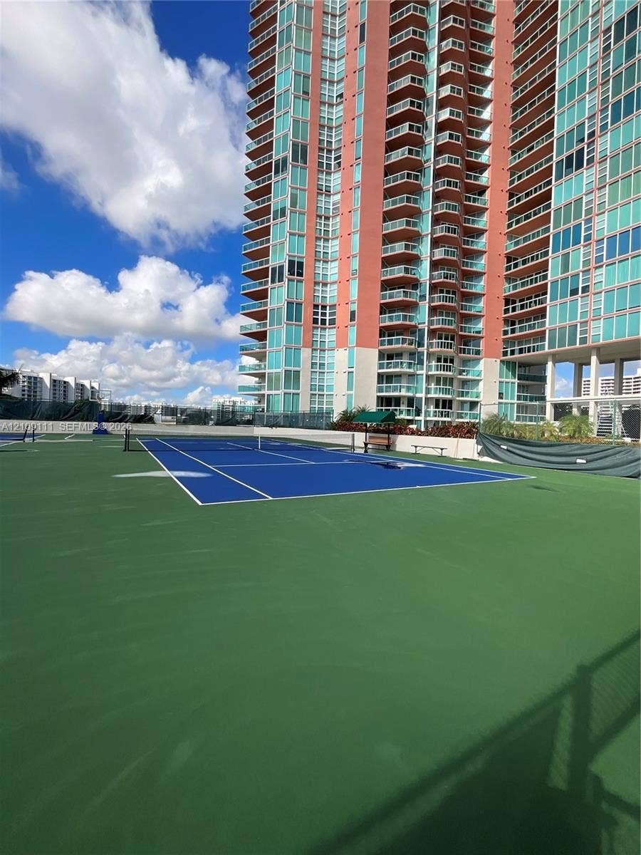 3370 Hidden Bay Drive, #801, Aventura, FL 33180 Recreational tennis court with blue and green surfacing, enclosed by high fencing and protective mesh screens