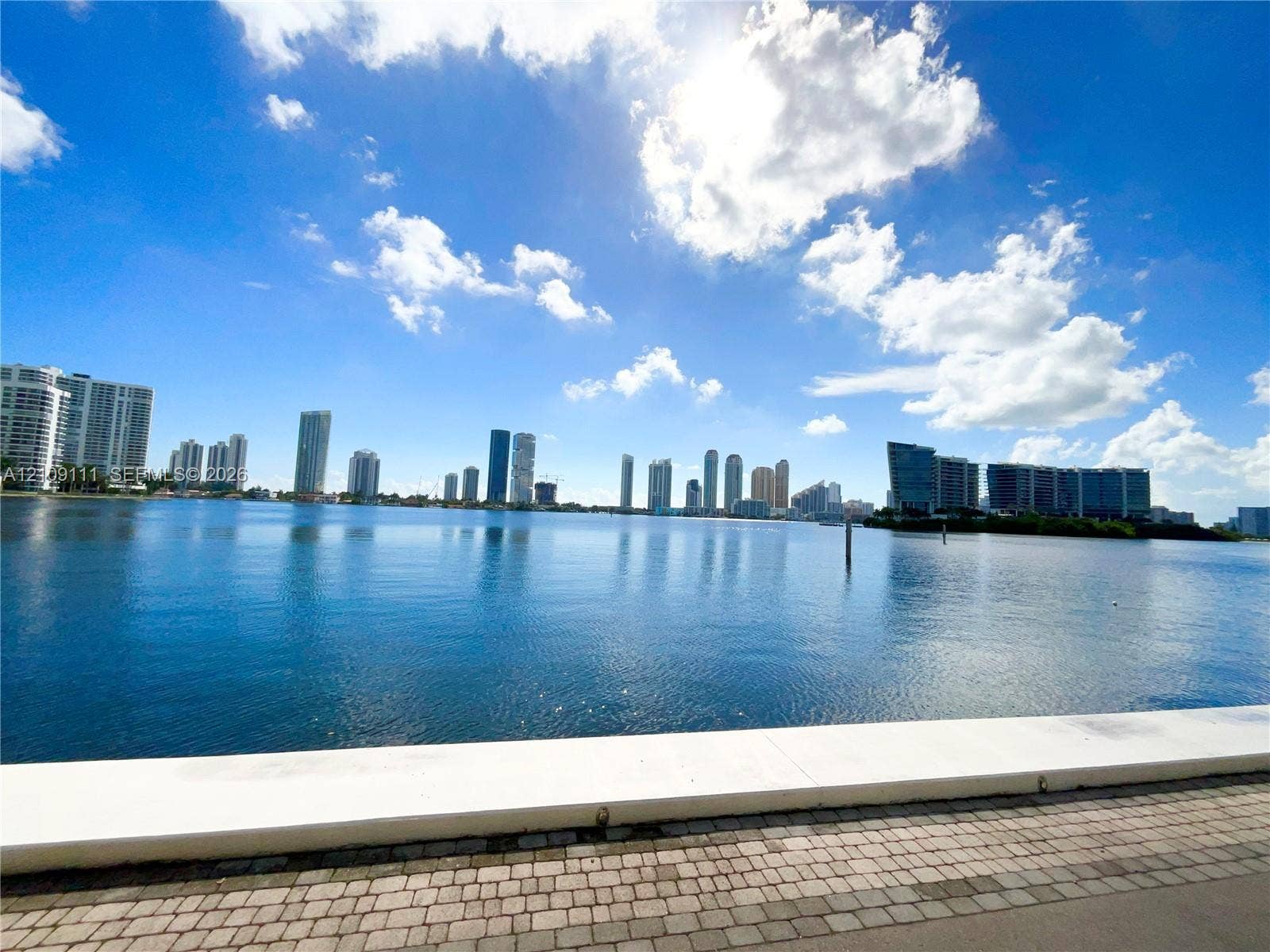3370 Hidden Bay Drive, #801, Aventura, FL 33180 Waterfront property featuring a concrete seawall, paver-lined walking path, and a backdrop of city skyline