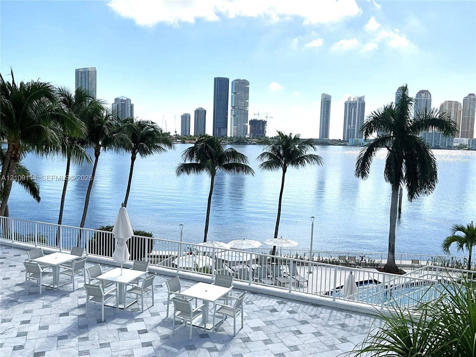 3370 Hidden Bay Drive, #801, Aventura, FL 33180 Expansive stone-paved terrace featuring metal railings, an integrated swimming pool, and mature palm trees with a backdrop of waterfront and city skyline