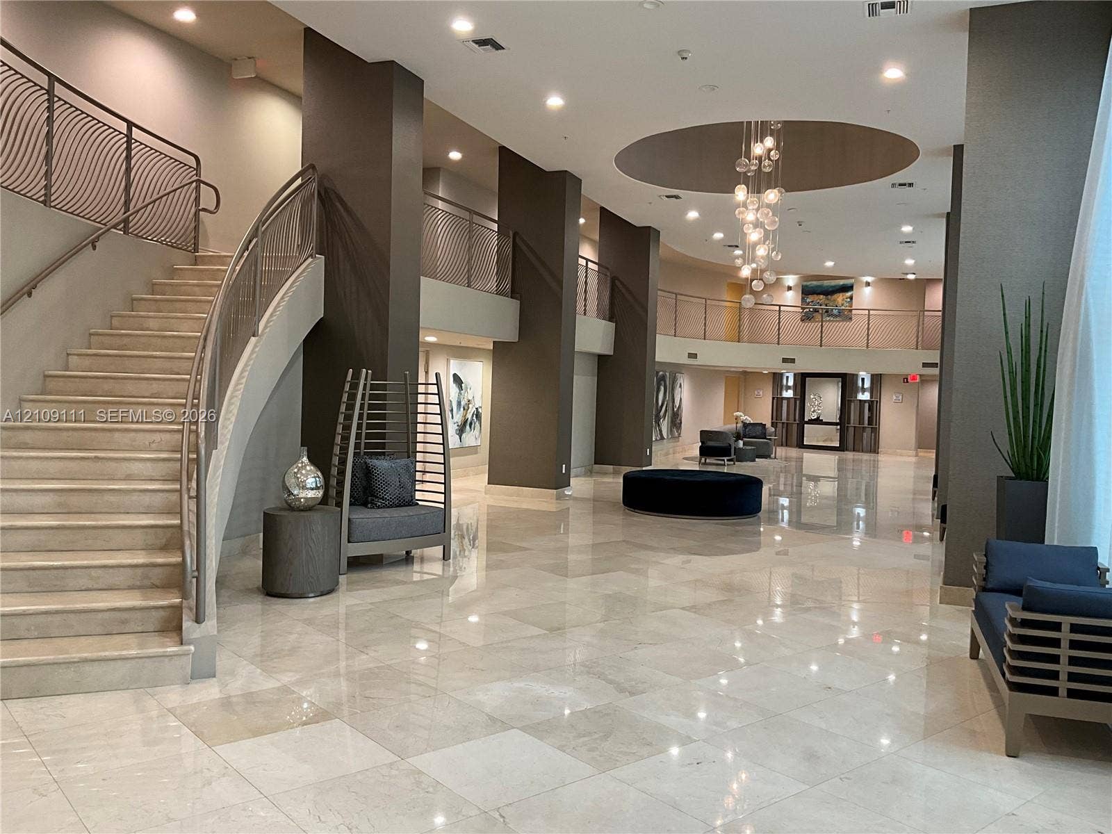 3370 Hidden Bay Drive, #801, Aventura, FL 33180 Grand lobby featuring polished stone flooring, a sweeping staircase with custom metal railing, vaulted ceiling with recessed lighting, and a multi-tiered decorative chandelier