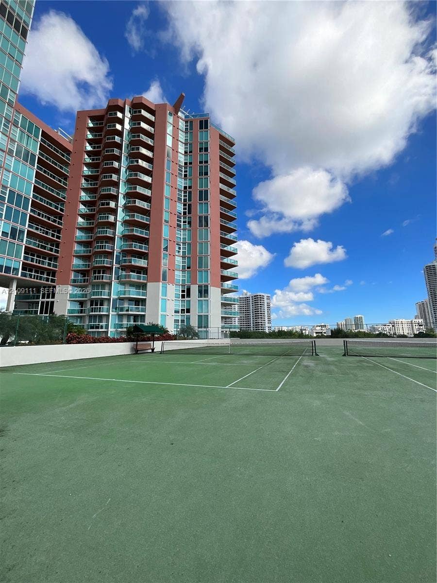 3370 Hidden Bay Drive, #801, Aventura, FL 33180 Tennis court with a green hard surface and white court markings, enclosed by chain-link fencing, situated on an outdoor elevated deck