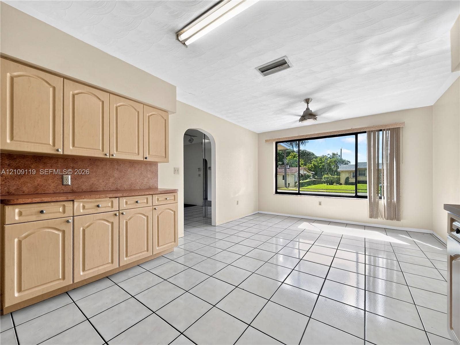Light wood-finish cabinetry, solid-surface countertops, ceramic tile flooring, arched entryway, and large picture window
