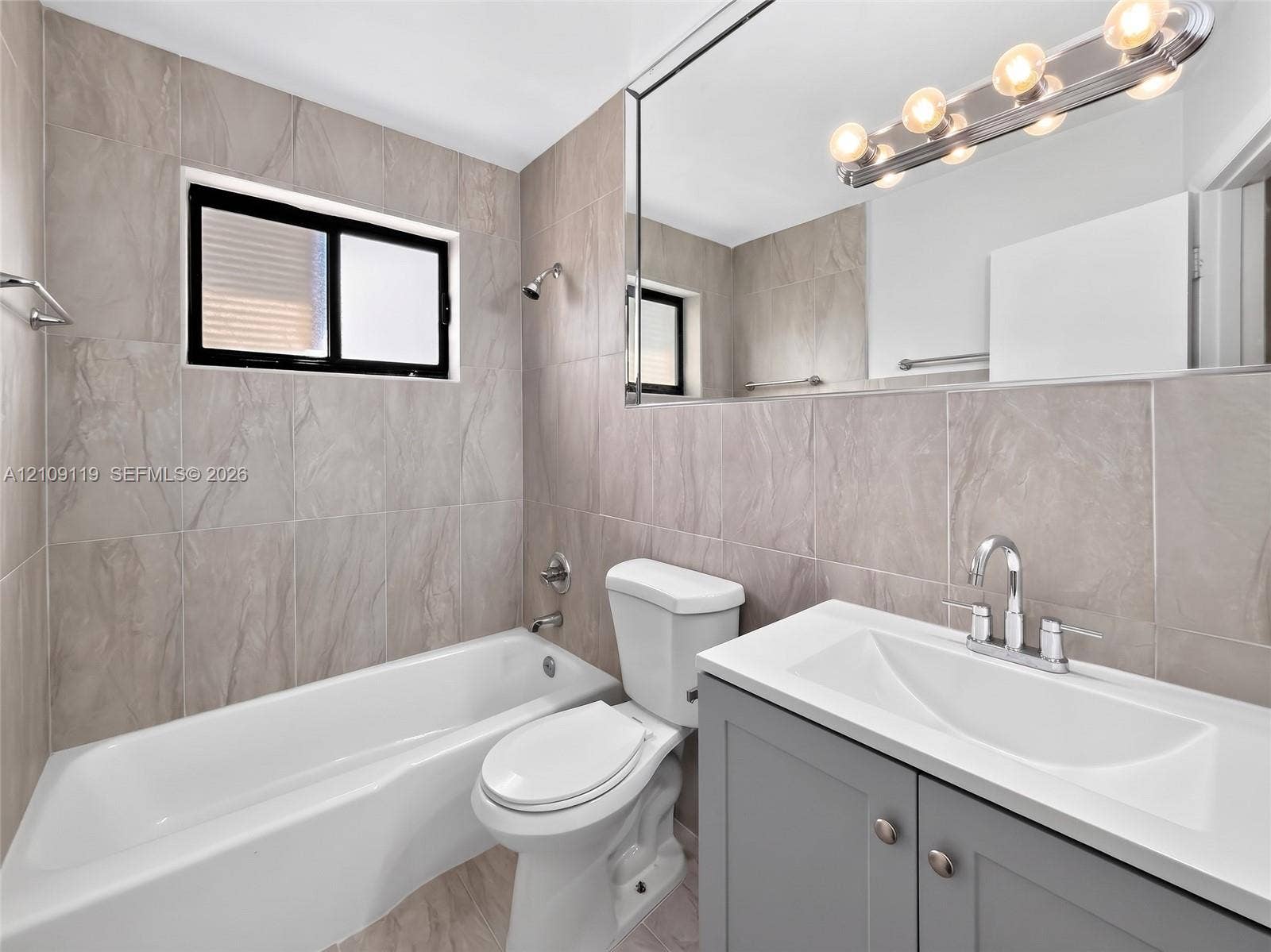Bathroom featuring floor-to-ceiling large-format tile, gray vanity with a white composite countertop, integrated sink, and full-width vanity mirror