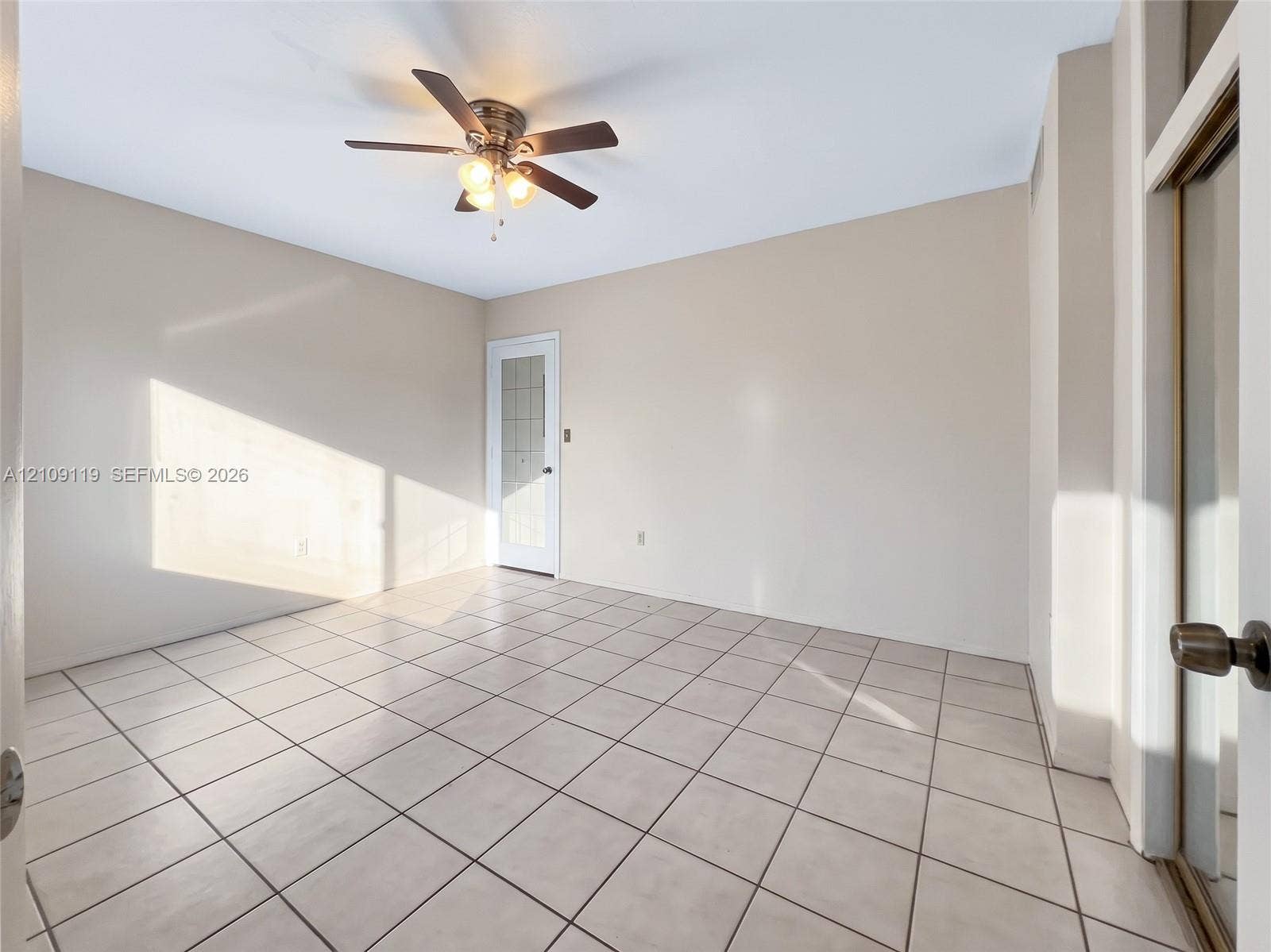 Neutral-toned interior space featuring light-colored square tile flooring, a multi-blade ceiling fan with integrated lighting, and a single-panel door with glass inserts