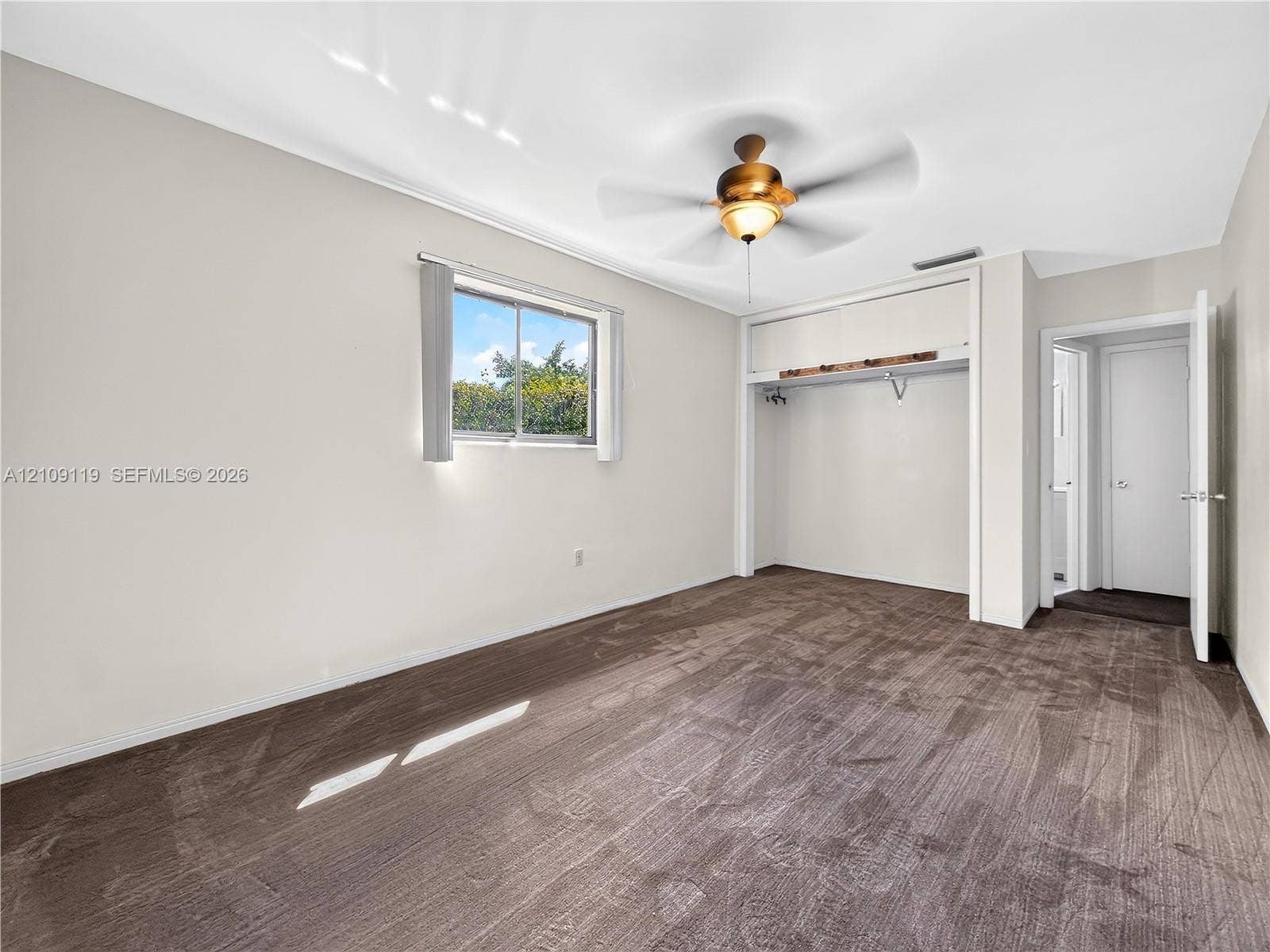 Neutral carpeting, recessed closet space with integrated shelving, sliding-sash window, and central ceiling fan with integrated light fixture