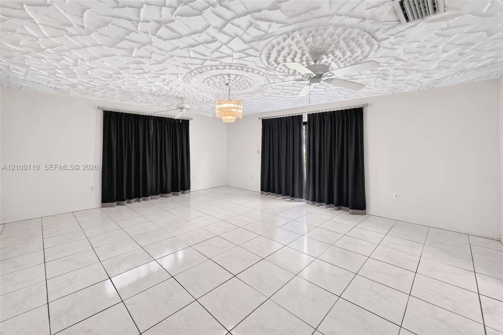 Expansive room featuring a textured decorative ceiling, dual ceiling fans, polished tile flooring, and a central tiered crystal chandelier