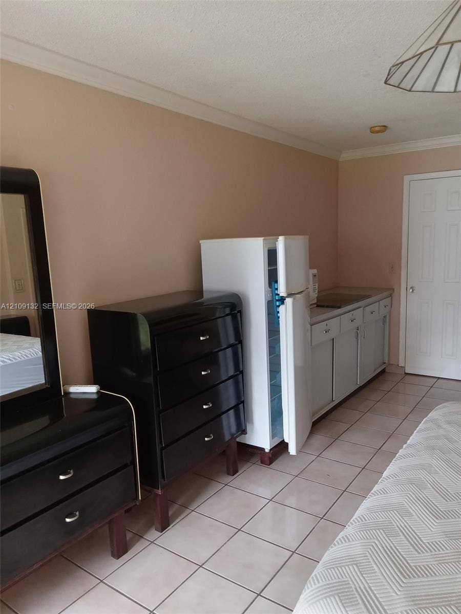Kitchenette area featuring light-toned cabinetry, a compact refrigerator, a recessed sink, and tile flooring