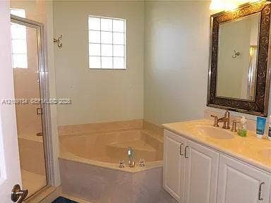 2529 SW Stockbridge Square SW, Vero Beach, FL 32962 Bathroom featuring a corner soaking tub, glass-enclosed shower, vanity with a stone countertop, and block-style privacy window
