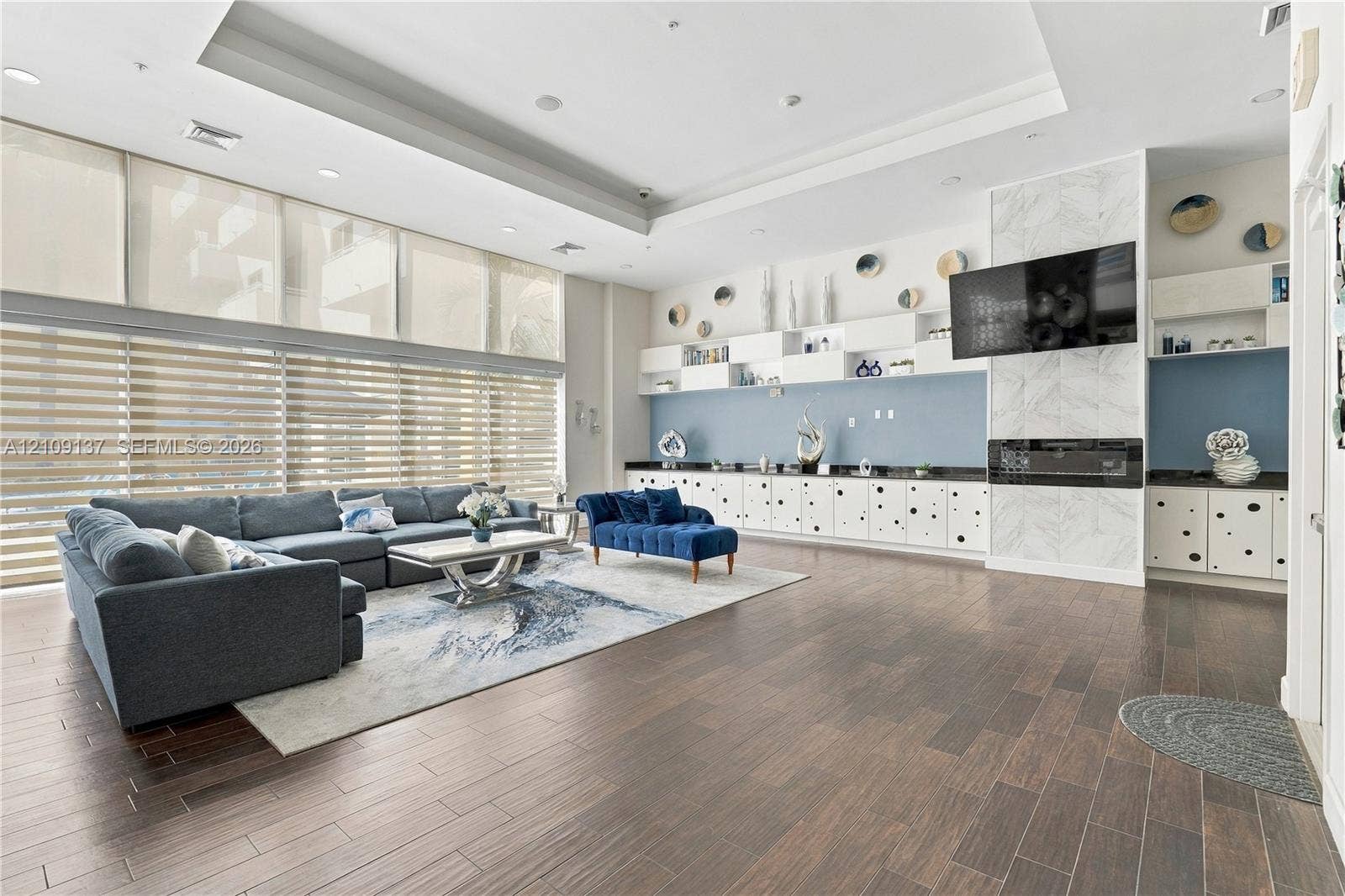 18800 NE 29th Avenue, #411, Aventura, FL 33180 Expansive living space featuring wood-finish flooring, floor-to-ceiling windows with roller shades, recessed tray ceilings, built-in cabinetry, and a fireplace with stone-finish surround