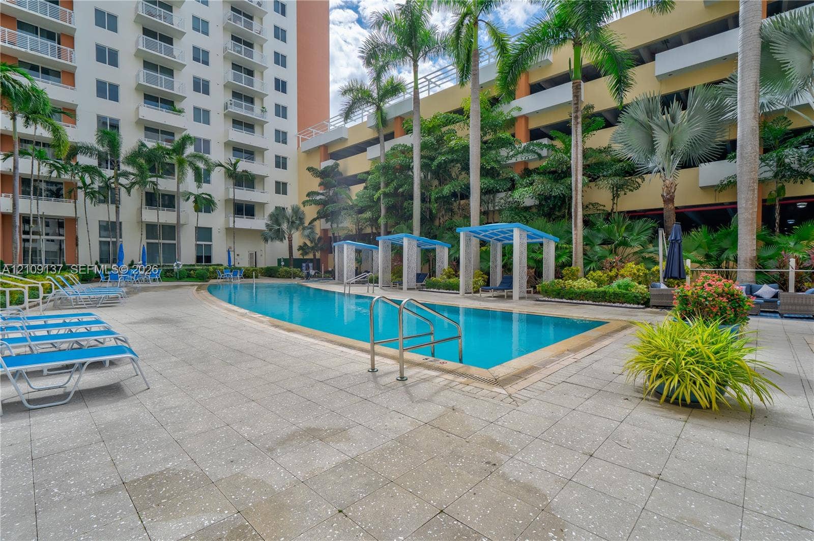 18800 NE 29th Avenue, #411, Aventura, FL 33180 Curved swimming pool with metal handrails, paved pool deck, and shaded pergola structures set among palm trees