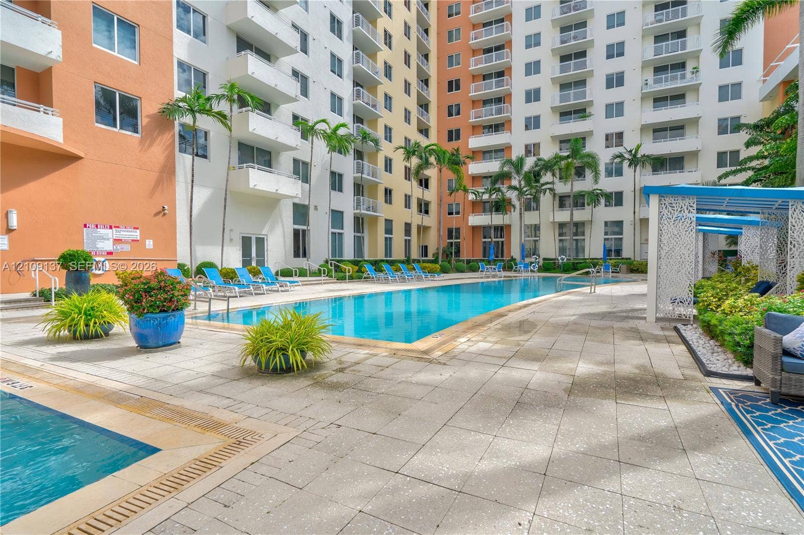 18800 NE 29th Avenue, #411, Aventura, FL 33180 Swimming pool area featuring a stone-paver pool deck, mature palm trees, multi-level exterior balconies, and a covered pergola structure
