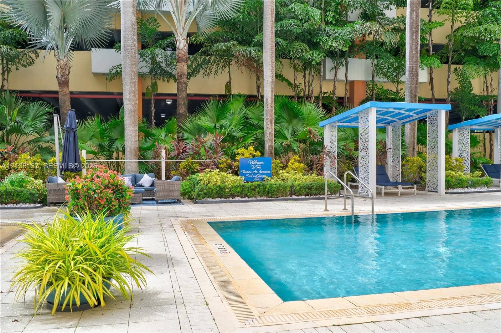 18800 NE 29th Avenue, #411, Aventura, FL 33180 Swimming pool with masonry coping, paver patio, and integrated shade structures surrounded by lush tropical landscaping
