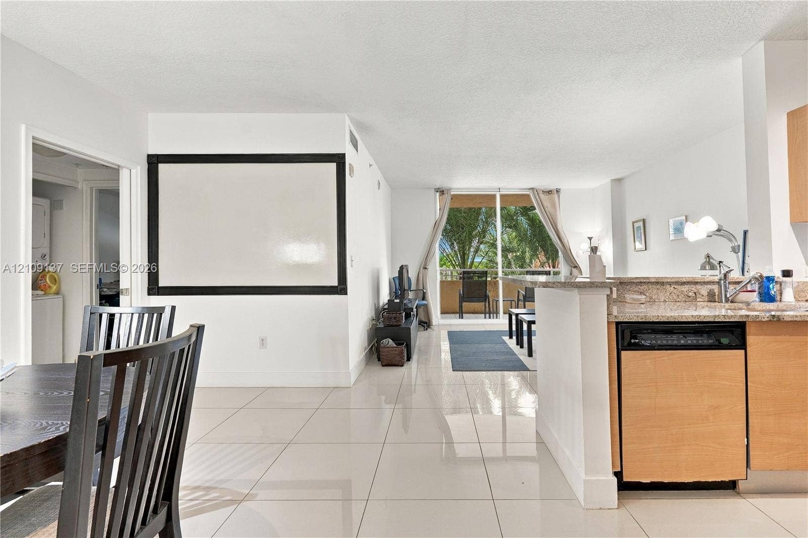 18800 NE 29th Avenue, #411, Aventura, FL 33180 Open-concept interior featuring light-toned tile flooring, kitchen with stone-finish countertops, wood-finish cabinetry, built-in dishwasher, and sliding glass doors to exterior balcony
