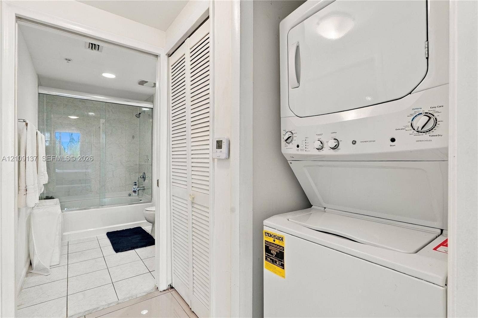 18800 NE 29th Avenue, #411, Aventura, FL 33180 Stacked laundry unit with white finish, closet with louvered doors, bathroom featuring a tub-shower combination with a glass enclosure, and ceramic tile flooring