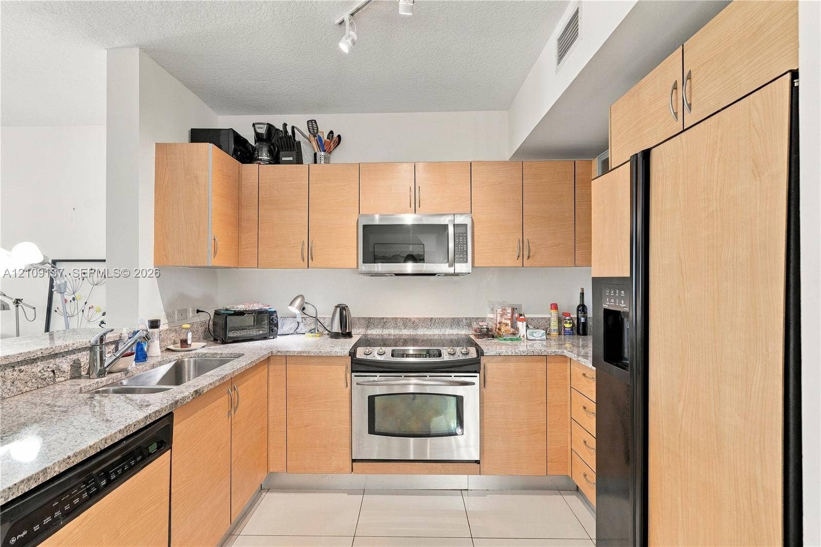18800 NE 29th Avenue, #411, Aventura, FL 33180 Kitchen featuring light-toned wood cabinetry, stone-surface countertops, stainless steel appliances, a dual-basin stainless steel sink, and tile flooring