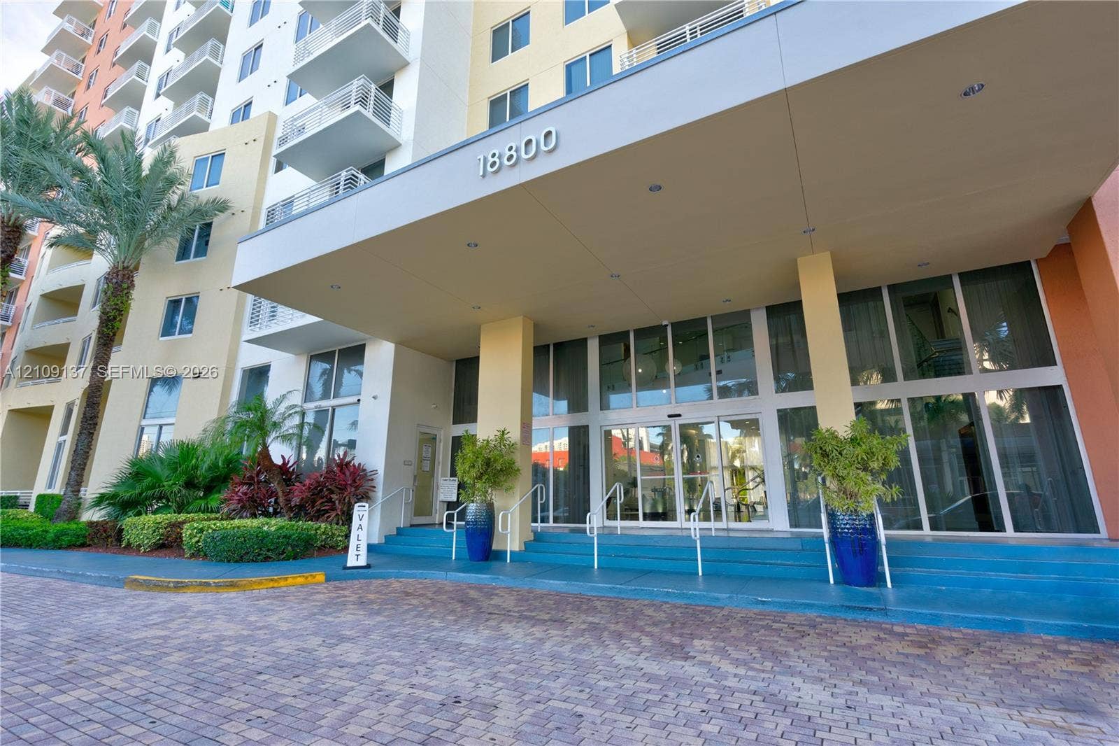 18800 NE 29th Avenue, #411, Aventura, FL 33180 Covered porte-cochre entry with paver driveway, expansive glass storefront entrance, and integrated landscaping