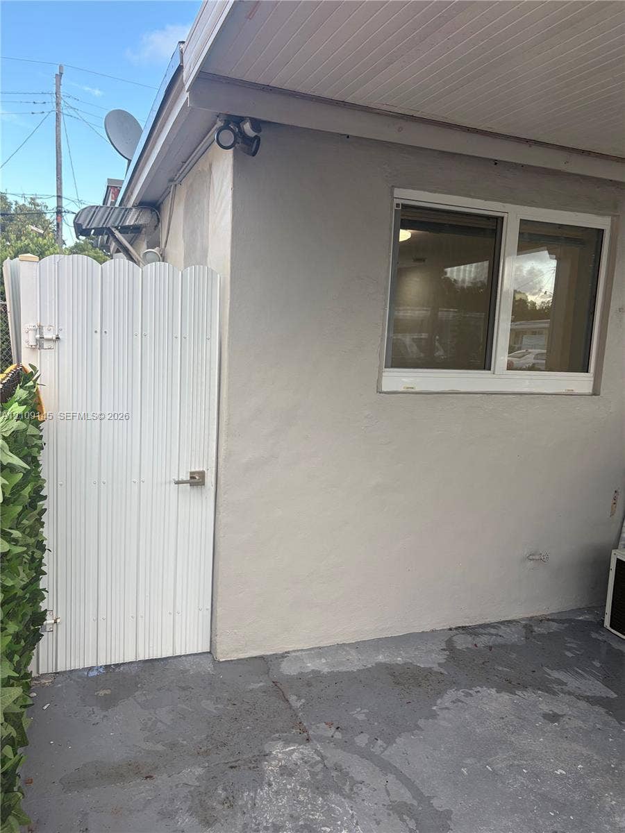 Exterior space featuring a white scalloped privacy gate, a sliding window with a white frame, and a covered entryway with a concrete surface