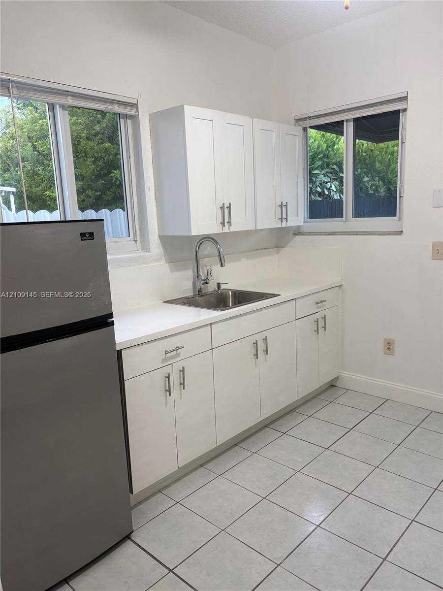 Kitchen featuring white cabinetry with stainless steel hardware, white countertops, a stainless steel undermount sink with a gooseneck faucet, ceramic tile flooring, and dual windows