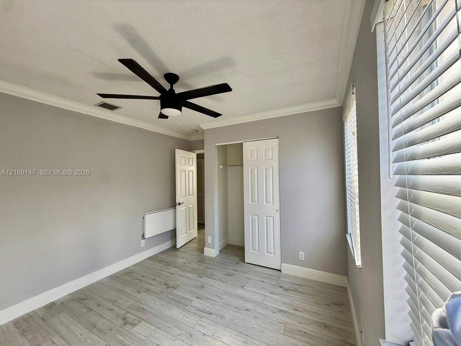 Room featuring wood-finish flooring, crown molding, a multi-blade ceiling fan, and a closet with a six-panel door