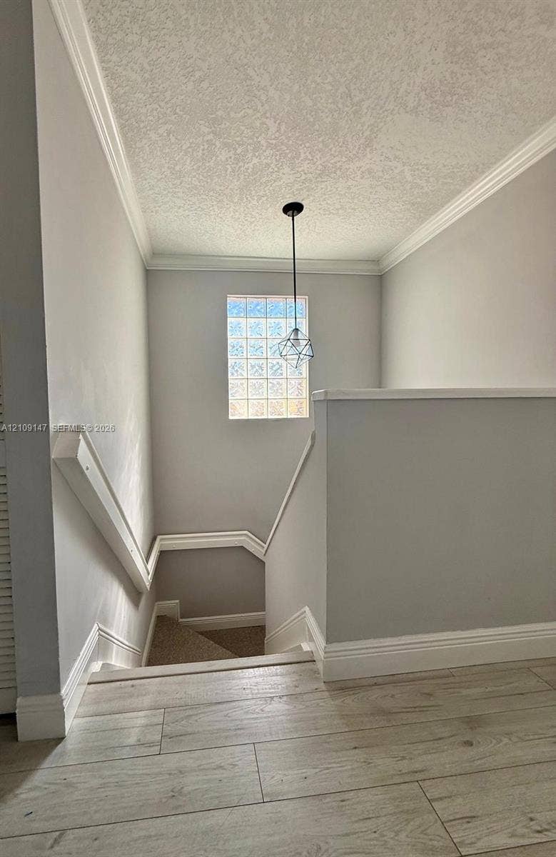 Wood-finish flooring, crown molding, glass block window, and geometric pendant lighting