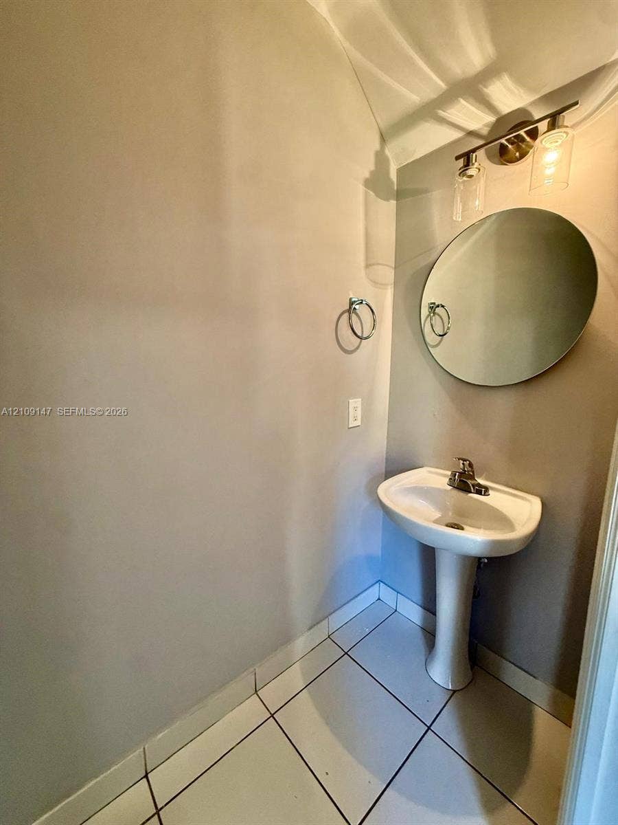 Pedestal sink with a center-set faucet, round frameless mirror, and three-light vanity fixture featuring cylindrical glass shades
