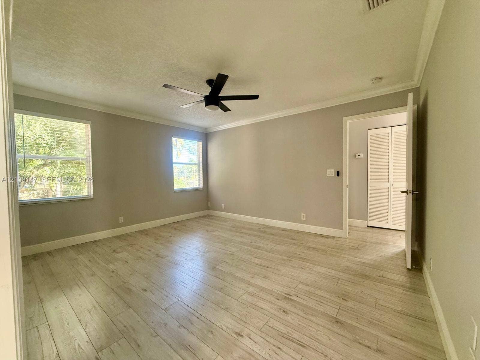 Interior room featuring wood-finish flooring, neutral wall paint, crown molding, a matte black ceiling fan, and louvered-style closet doors