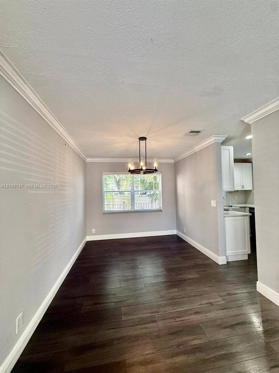 Dining area featuring wood-finish flooring, crown molding, a central chandelier, and a large window