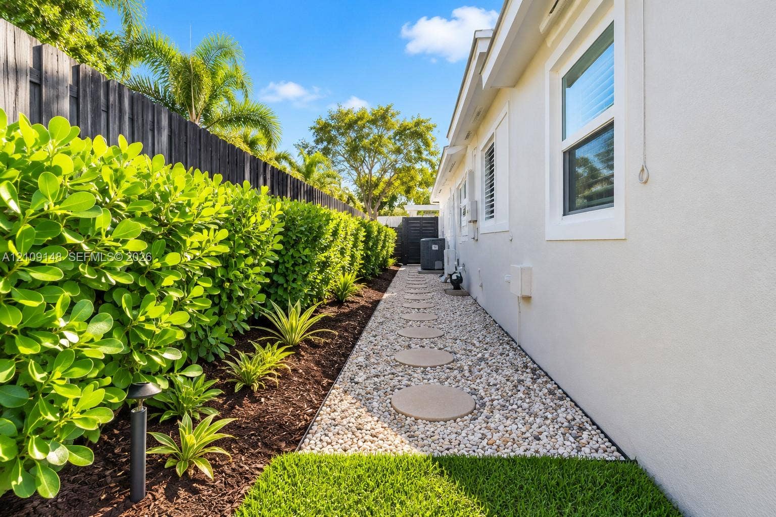 1701 SW 23rd Avenue, Fort Lauderdale, FL 33312 Side yard featuring a stone pathway, privacy fencing, manicured hedges, and professional landscape beds with mulch