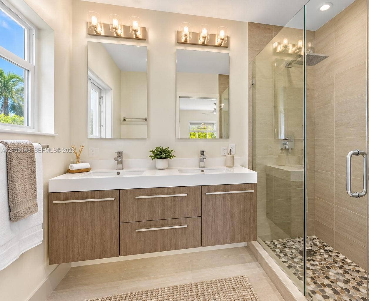 1701 SW 23rd Avenue, Fort Lauderdale, FL 33312 Dual-sink vanity with wood-finish cabinetry, quartz countertop, framed glass shower enclosure, stone pebble shower flooring, and wall-mounted vanity lighting