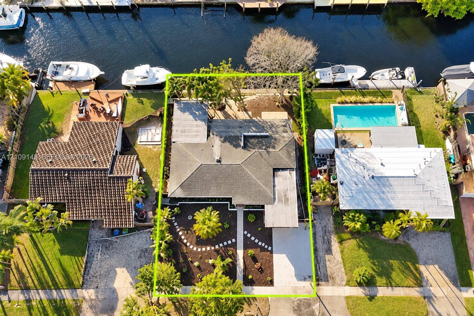 1701 SW 23rd Avenue, Fort Lauderdale, FL 33312 Waterfront property featuring a private bulkhead, canal access, a concrete driveway, and landscape beds with mature palm trees