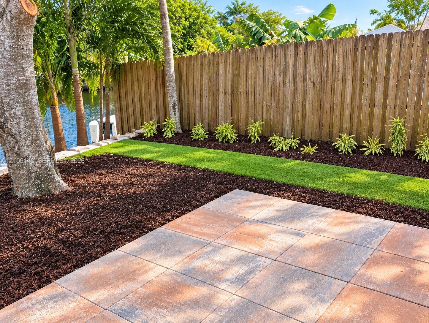 1701 SW 23rd Avenue, Fort Lauderdale, FL 33312 Backyard featuring large-format paver patio, manicured lawn, mulched garden beds, and perimeter wood fencing