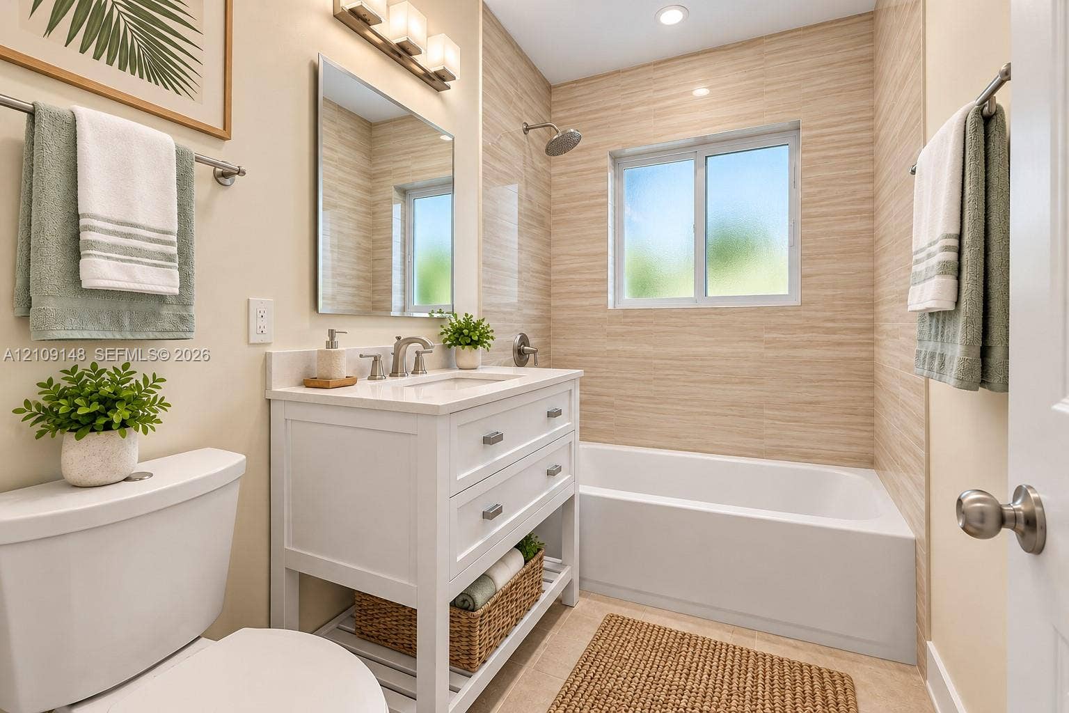 1701 SW 23rd Avenue, Fort Lauderdale, FL 33312 White vanity with dual soft-close drawers and an open lower shelf, rectangular sink with polished chrome hardware, framed mirror with three-light vanity bar fixture, and floor-to-ceiling textured tile surrounding a built-in soaking tub