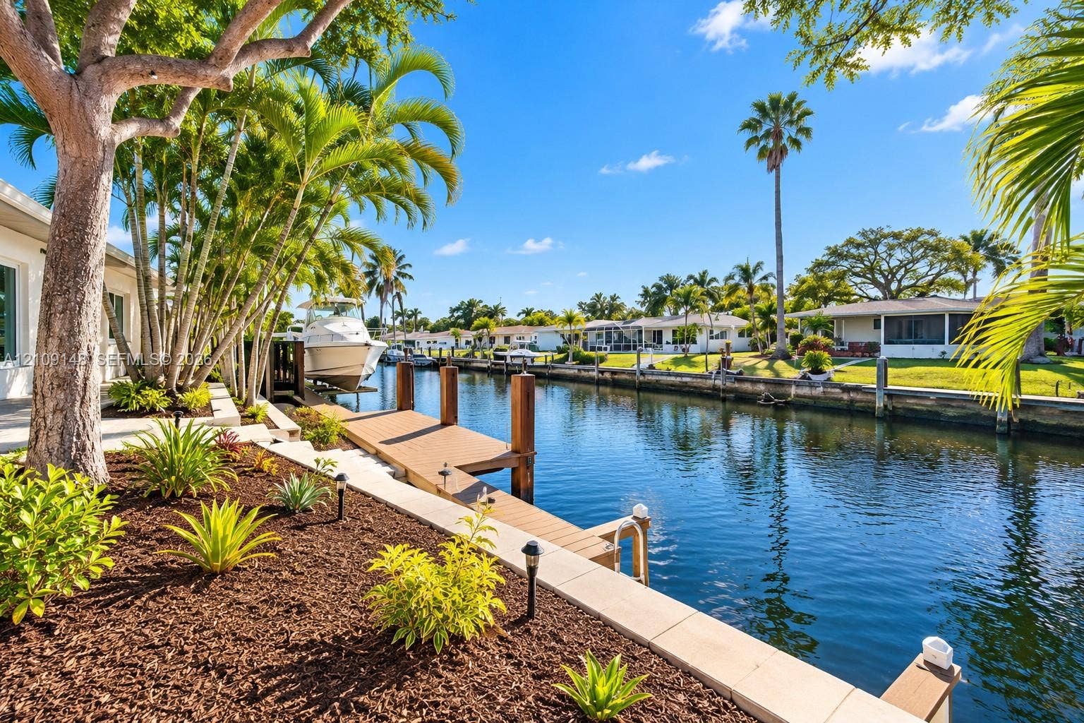 1701 SW 23rd Avenue, Fort Lauderdale, FL 33312 Waterfront property featuring a private wooden dock, concrete seawall, tiered landscaping with mulch beds, and mature palm trees