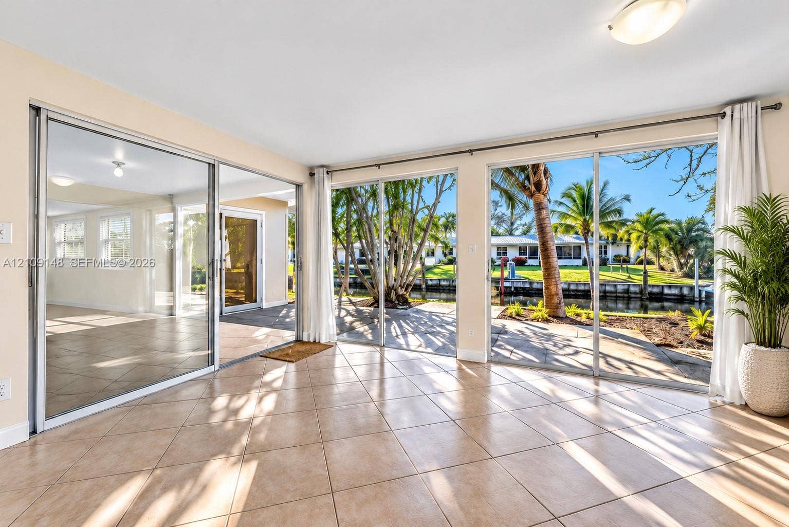 1701 SW 23rd Avenue, Fort Lauderdale, FL 33312 Expansive room featuring wall-to-wall sliding glass doors, neutral tile flooring, and direct access to a waterfront patio with palm trees
