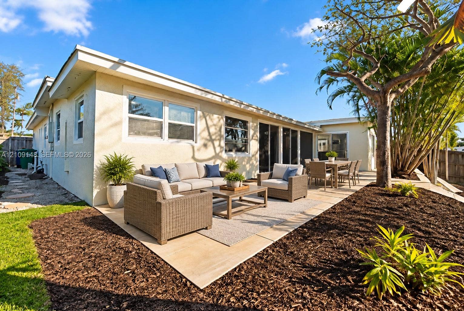 1701 SW 23rd Avenue, Fort Lauderdale, FL 33312 Rear exterior featuring a stucco facade, expansive paved patio, mature trees, and sliding glass door access