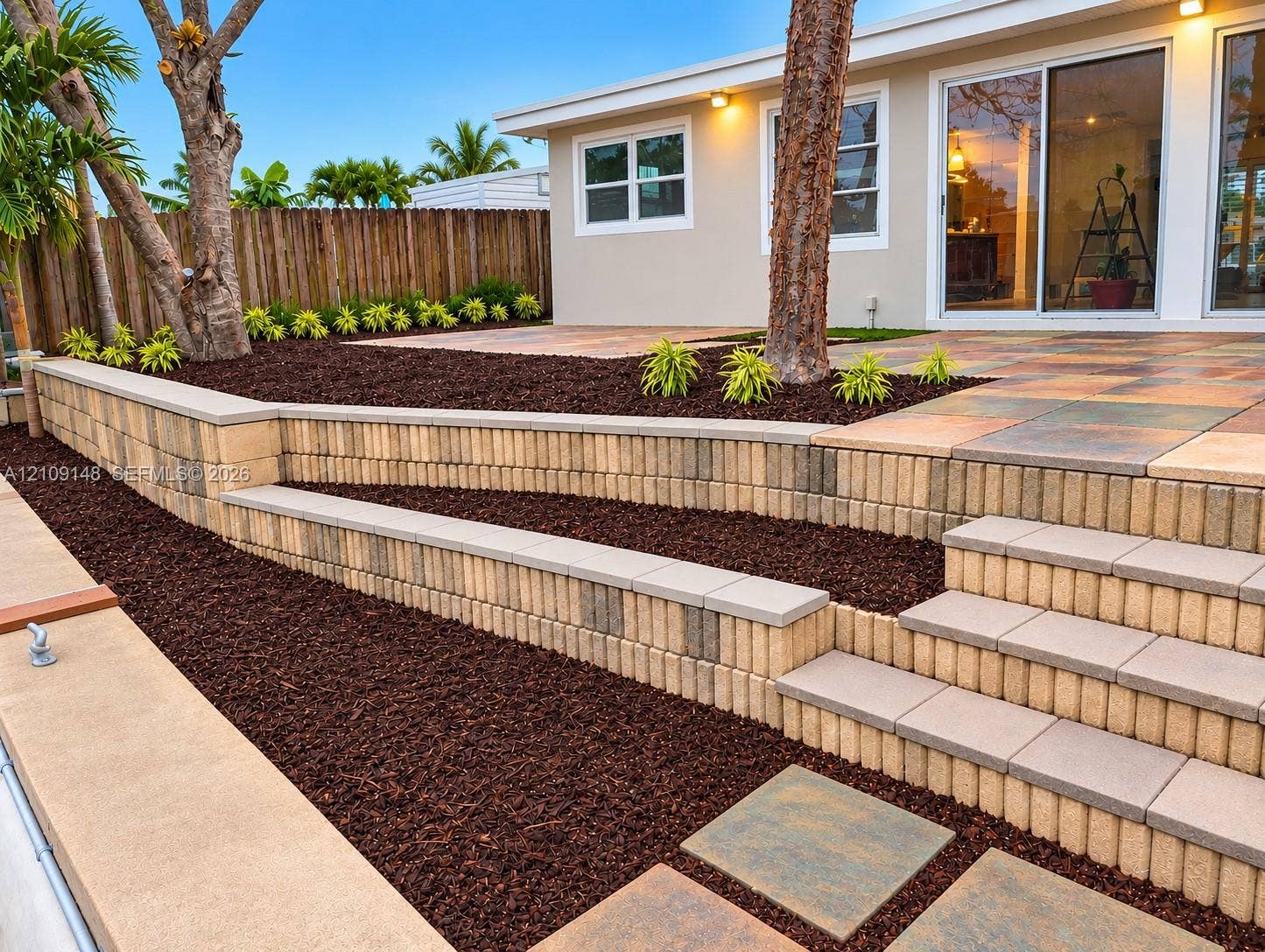 1701 SW 23rd Avenue, Fort Lauderdale, FL 33312 Terraced backyard featuring multi-level retaining walls, integrated staircases, large-format paver patio, wood-finish privacy fencing, and mulched landscaping beds