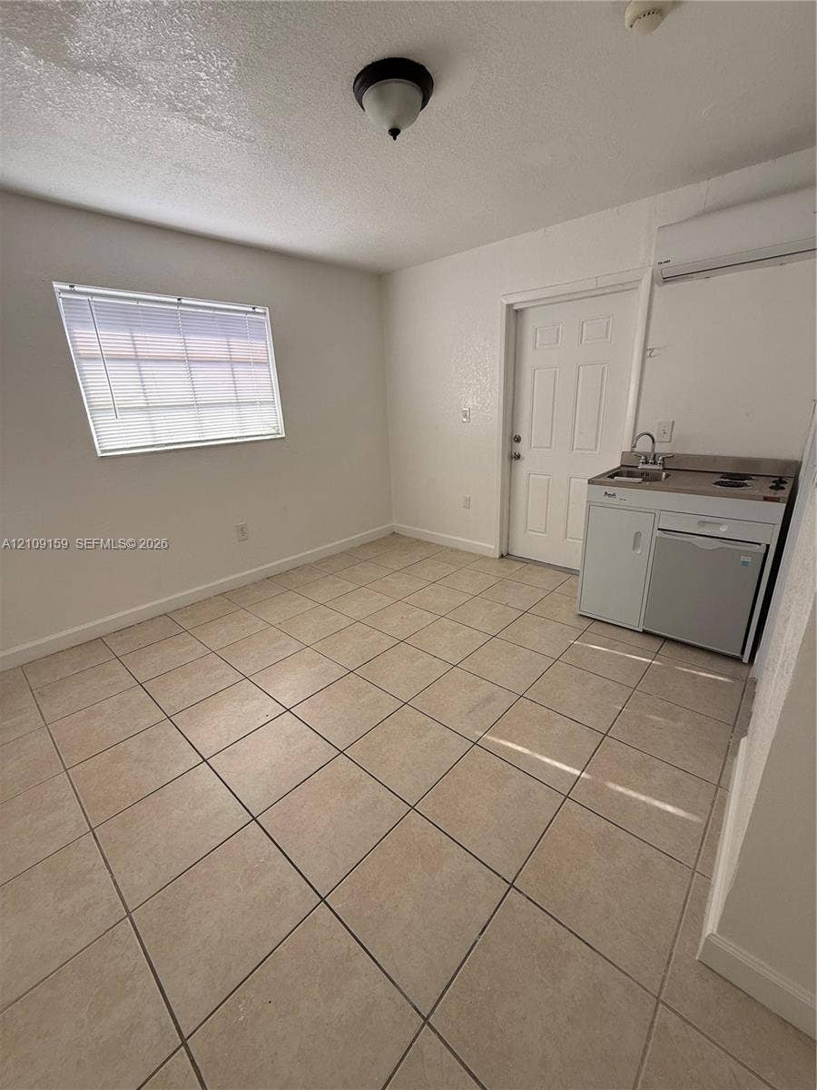 Ceramic tile flooring, white walls, and a compact kitchenette featuring a sink, two-burner cooktop, and under-counter appliance