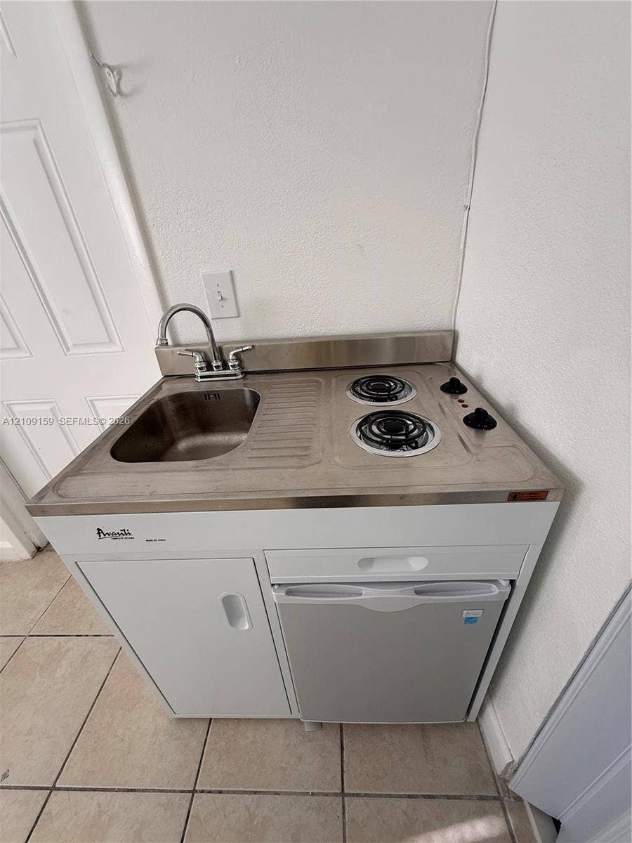 Compact kitchenette unit featuring a stainless steel integrated sink and dual-burner electric cooktop, white cabinetry, and a built-in under-counter refrigerator