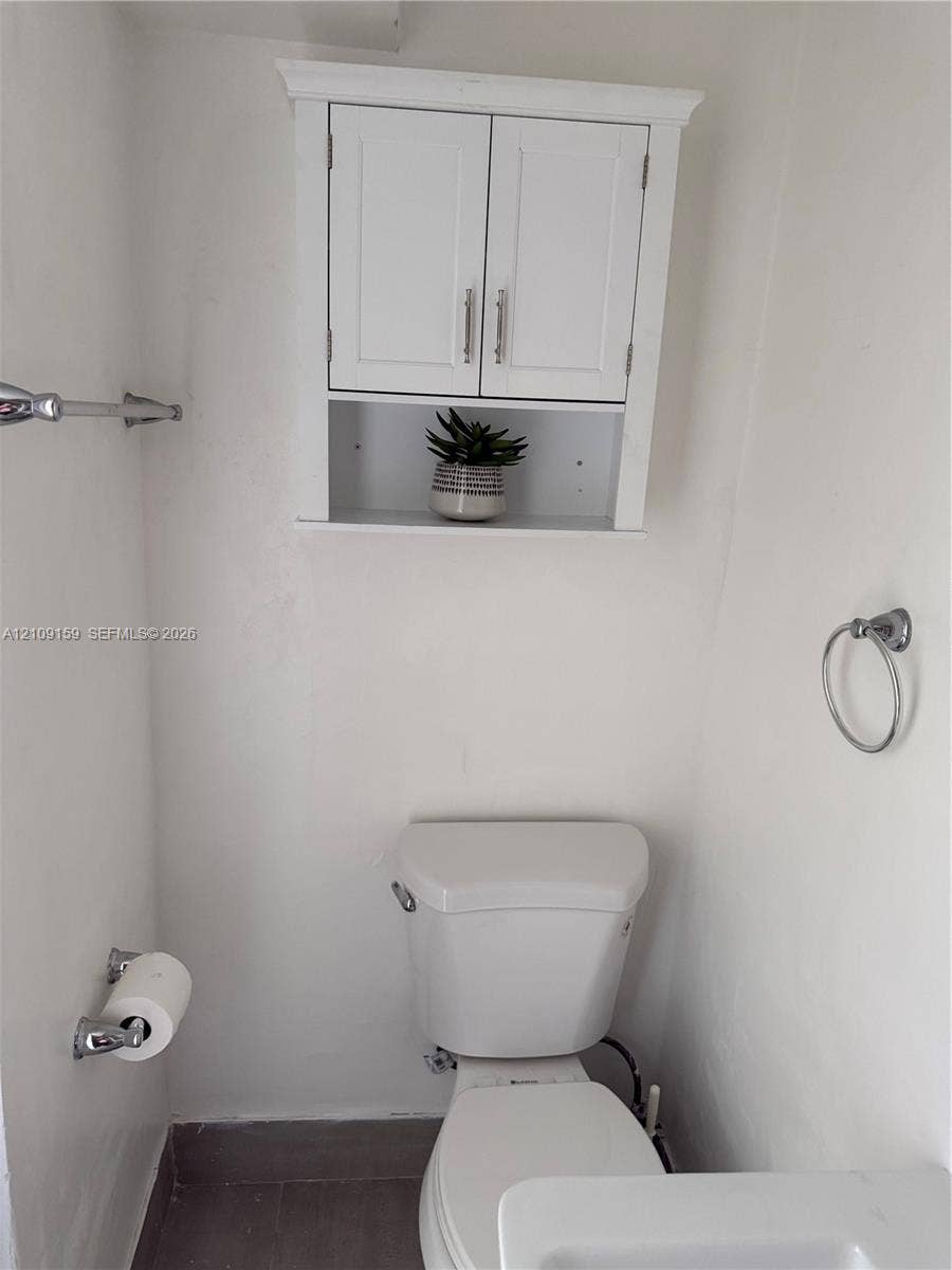 Wall-mounted white cabinetry featuring double doors and an open storage shelf, complemented by chrome hardware including a towel bar and circular ring