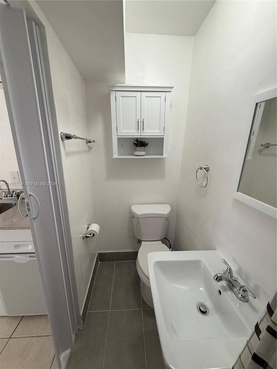 Wall-mounted white cabinetry, pedestal sink with chrome faucet, large-format grey tile flooring, and matching chrome hardware fixtures