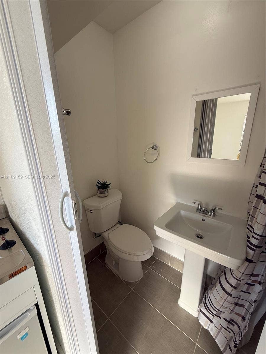 Bathroom featuring tile flooring, a white pedestal sink, a dual-handle faucet, and a wall-mounted mirror
