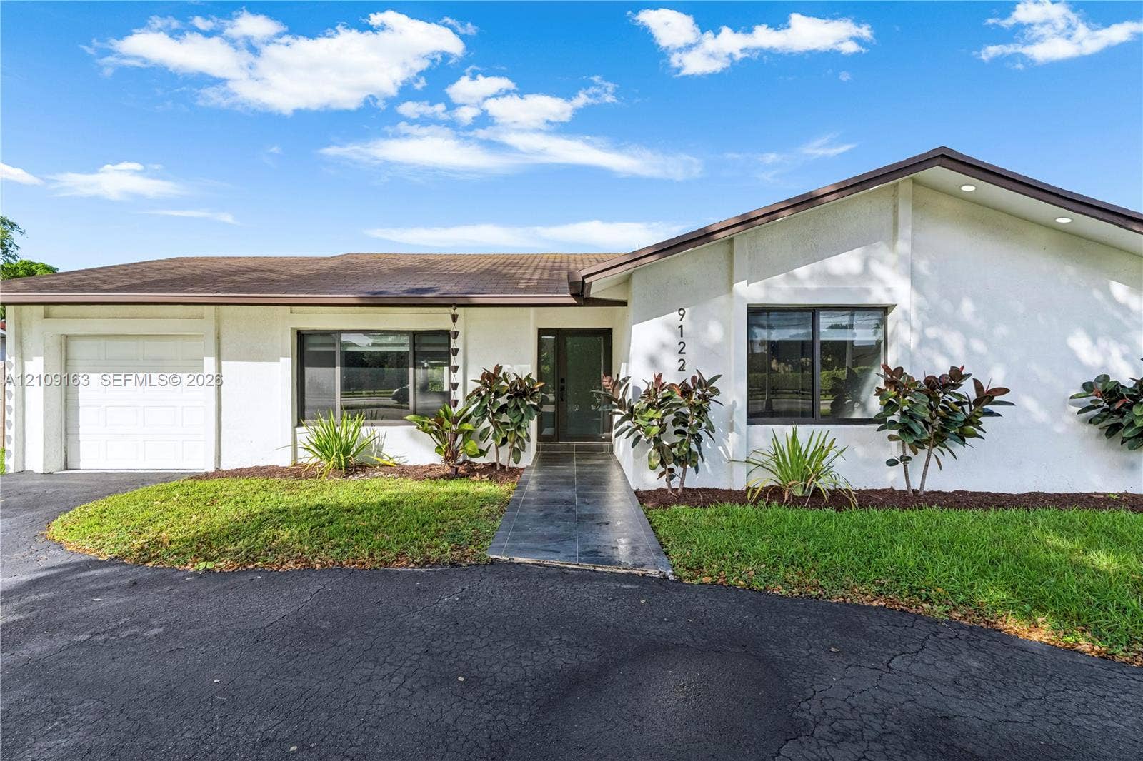 9122 SW 127th Avenue, Miami, FL 33186 Single-story exterior featuring white stucco siding, a tiled roof, a paved walkway, a multi-pane glass entry door, and an attached garage