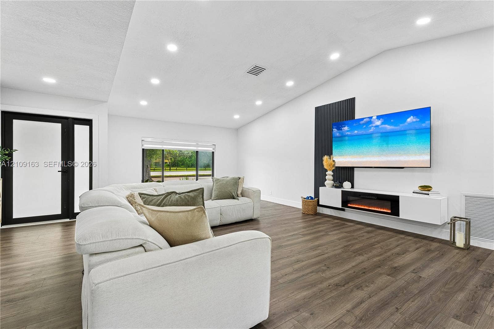 9122 SW 127th Avenue, Miami, FL 33186 Vaulted ceilings with recessed lighting, wood-finish flooring, a black vertical-slatted accent wall, and a wall-mounted floating media console with an integrated electric fireplace
