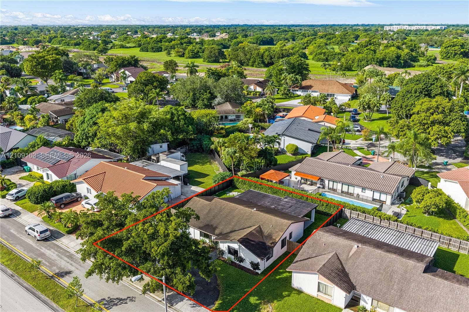 9122 SW 127th Avenue, Miami, FL 33186 Aerial perspective of a property featuring a single-story residence, asphalt driveway, manicured lawn, and mature trees enclosed by perimeter hedging