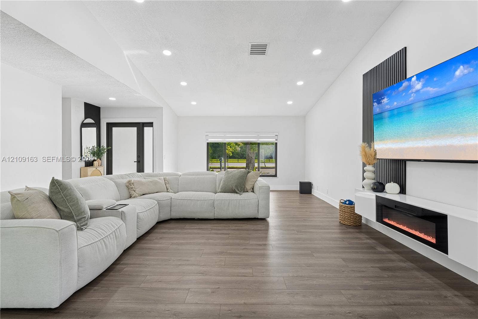 9122 SW 127th Avenue, Miami, FL 33186 Wood-finish flooring, recessed lighting, wall-mounted linear electric fireplace, vertical slat accent wall, and glass-paneled exterior door