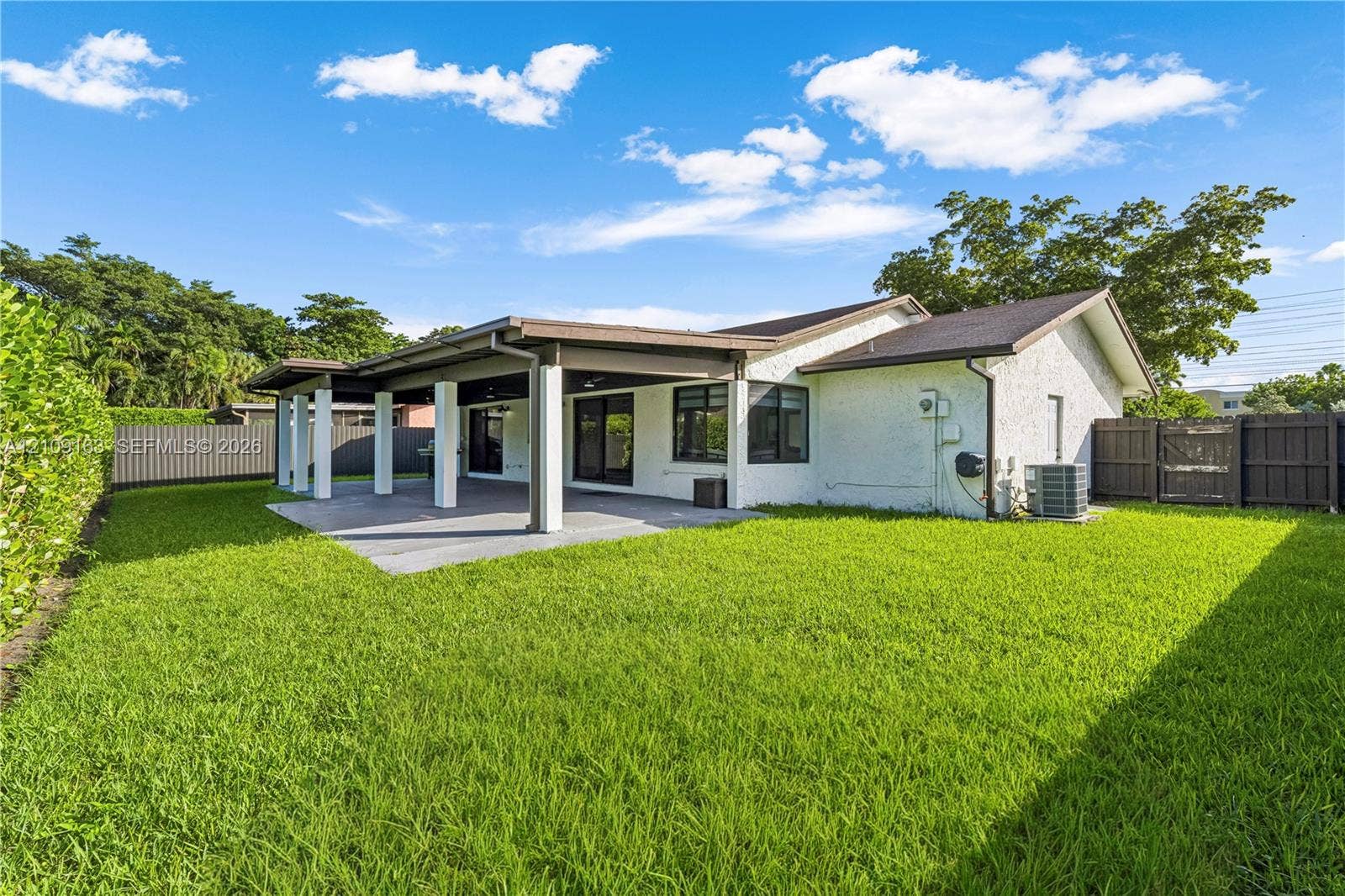 9122 SW 127th Avenue, Miami, FL 33186 Expansive backyard featuring a manicured lawn, a covered concrete patio with structural columns, and enclosed perimeter fencing