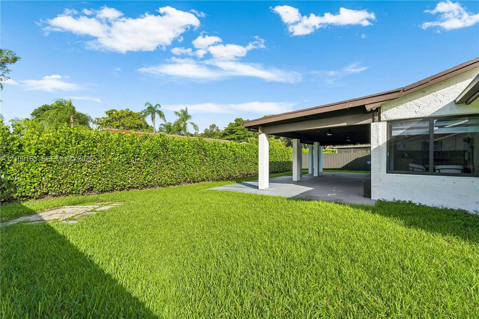 9122 SW 127th Avenue, Miami, FL 33186 Rear yard featuring a manicured lawn, paved covered patio, stucco exterior finish, and dense perimeter hedging