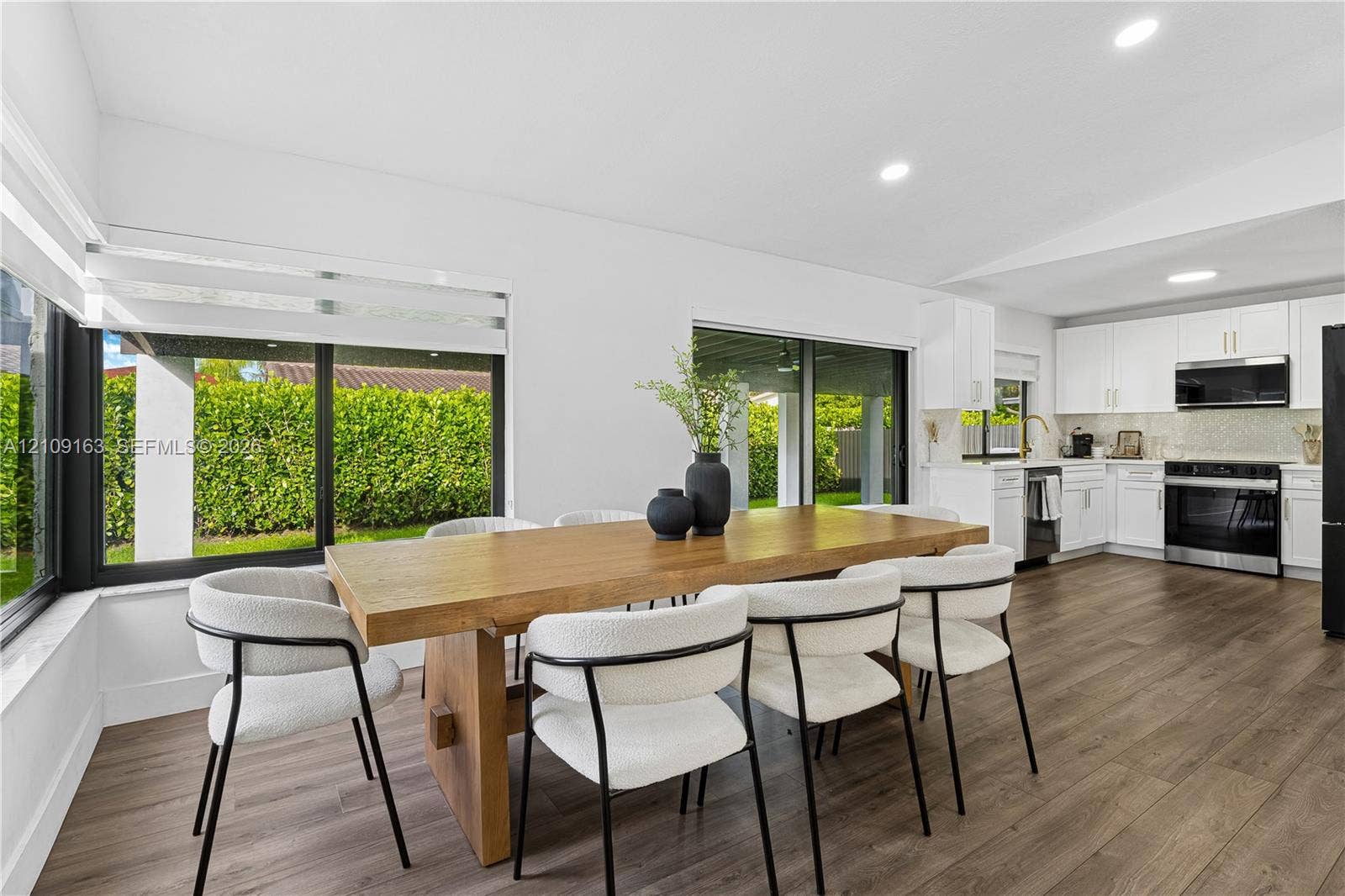 9122 SW 127th Avenue, Miami, FL 33186 Open-concept kitchen and dining area featuring wood-finish flooring, recessed lighting, white shaker-style cabinetry, and large sliding glass doors