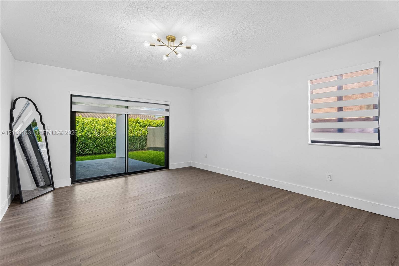 9122 SW 127th Avenue, Miami, FL 33186 Spacious room featuring wood-finish flooring, a modern sputnik-style ceiling light fixture, sliding glass doors, and dual-layered window shades