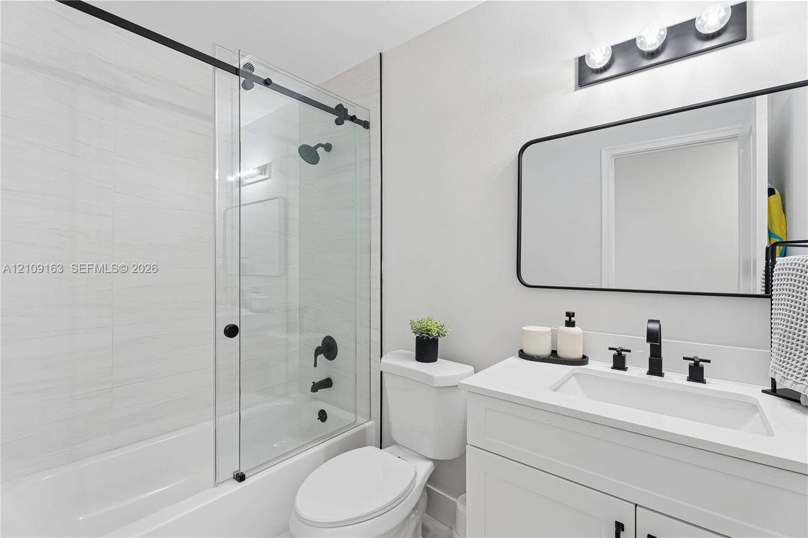 9122 SW 127th Avenue, Miami, FL 33186 Bathroom featuring a vanity with a white countertop and rectangular undermount sink, a glass sliding shower door with matte black hardware, horizontal wall tile, and a rectangular mirror with a black frame